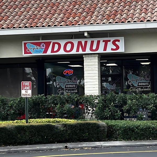 Exterior view of Jupiter Donuts storefront with a red tile roof and an "OPEN" sign.