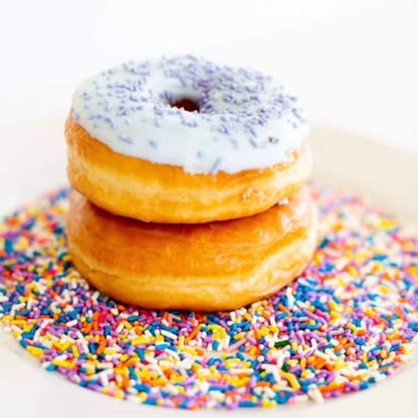 Two stacked donuts, one with light blue icing and purple sprinkles, on a bed of colorful sprinkles.