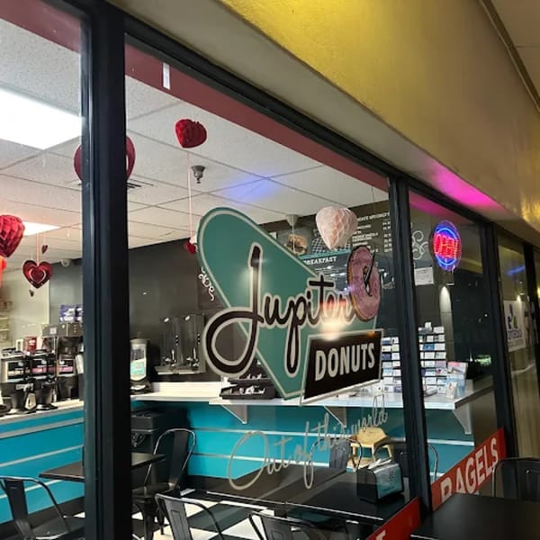 The exterior of Jupiter Donuts, featuring a retro-style sign and heart decorations visible through the window.