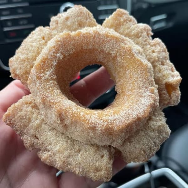 A hand holds a cinnamon sugar-dusted donut with a car interior in the blurred background.