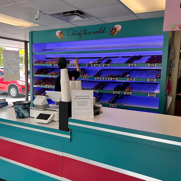 A Jupiter Donuts employee behind the counter, stocking shelves of donuts under blue lights.
