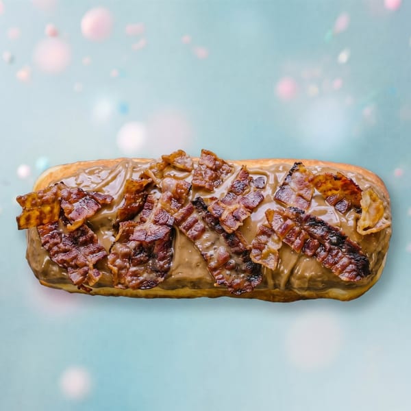 Long john donut with maple frosting and crispy bacon bits on a light blue background.