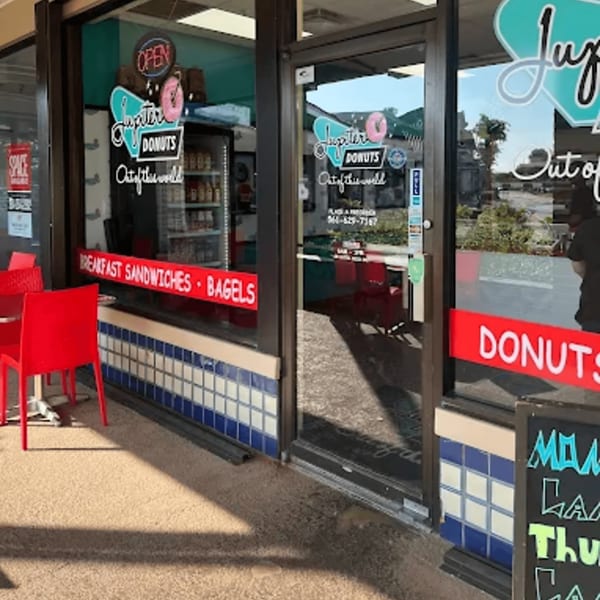 Exterior of Jupiter Donuts with red chairs outside, showcasing window signage for donuts and breakfast items.