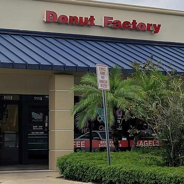 Exterior of Jupiter Donuts, with a red "Donut Factory" sign and a blue awning.