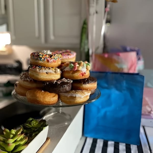 A glass stand piled high with assorted Jupiter Donuts, including chocolate, sprinkles, and cereal toppings.