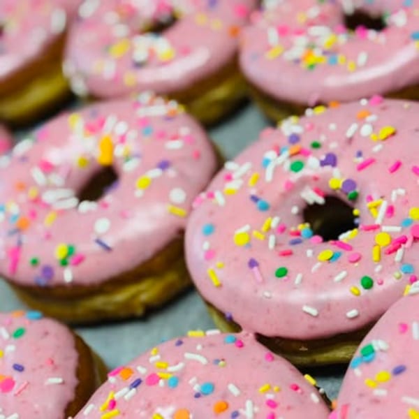 Close-up of multiple pink-frosted donuts with colorful sprinkles, arranged on a tray.