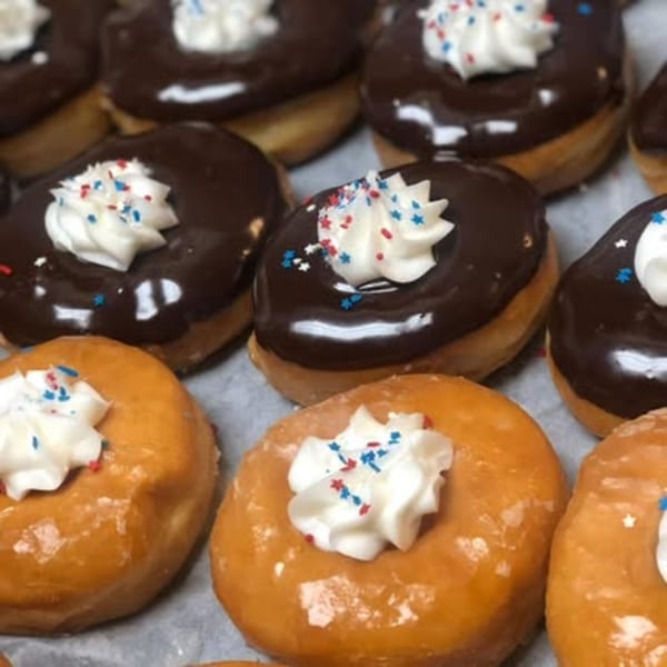 Rows of chocolate and glazed donuts topped with whipped cream and patriotic sprinkles.