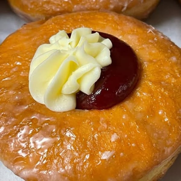 Close-up of a glazed donut with a dollop of white cream and a spoonful of red jam.